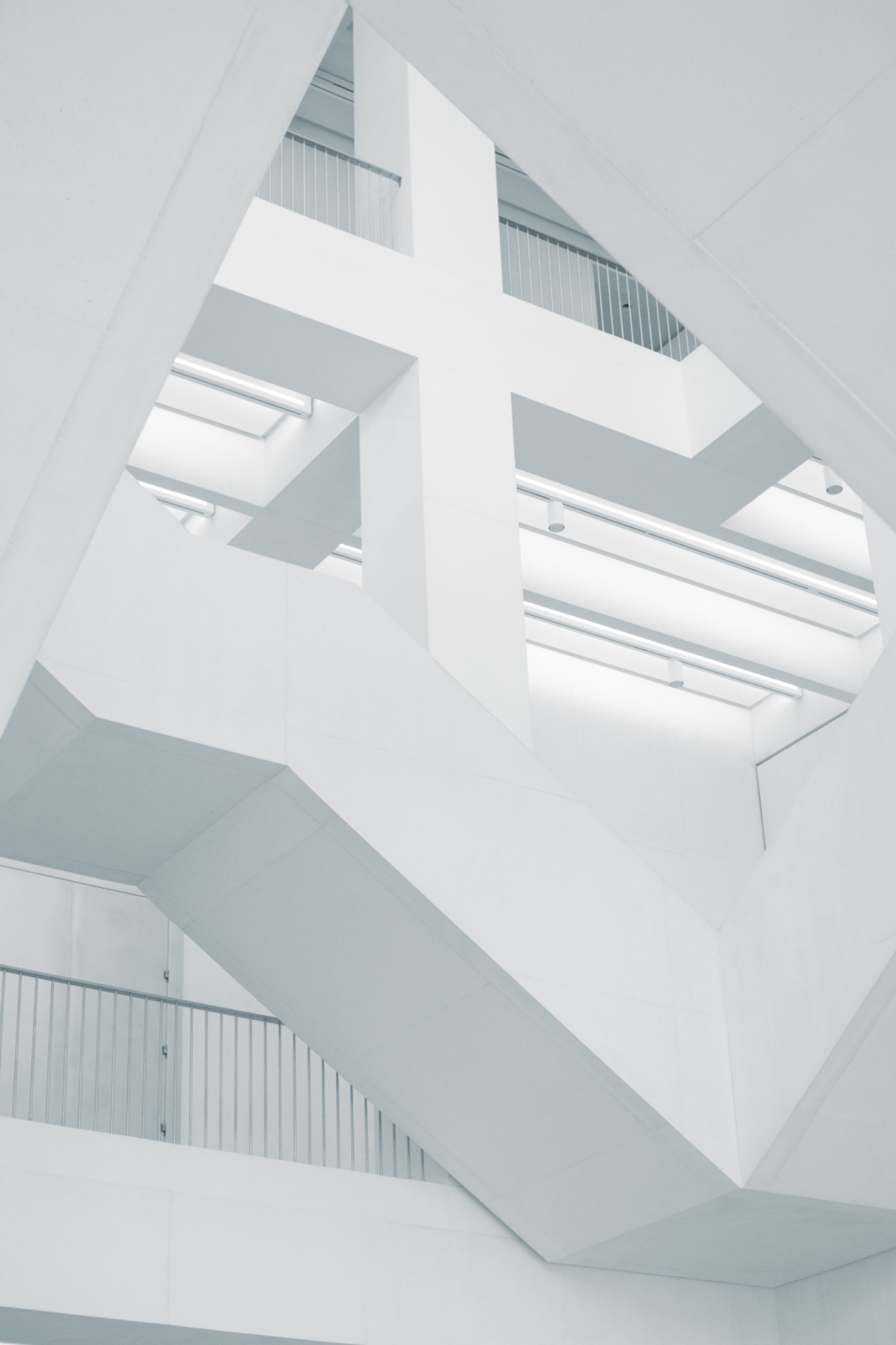 Minimalistyczne wnętrze: białe, geometryczne schody i balustrady. Ujęcie z dołu, podkreślające architektoniczny detal i oświetlenie sufitowe.