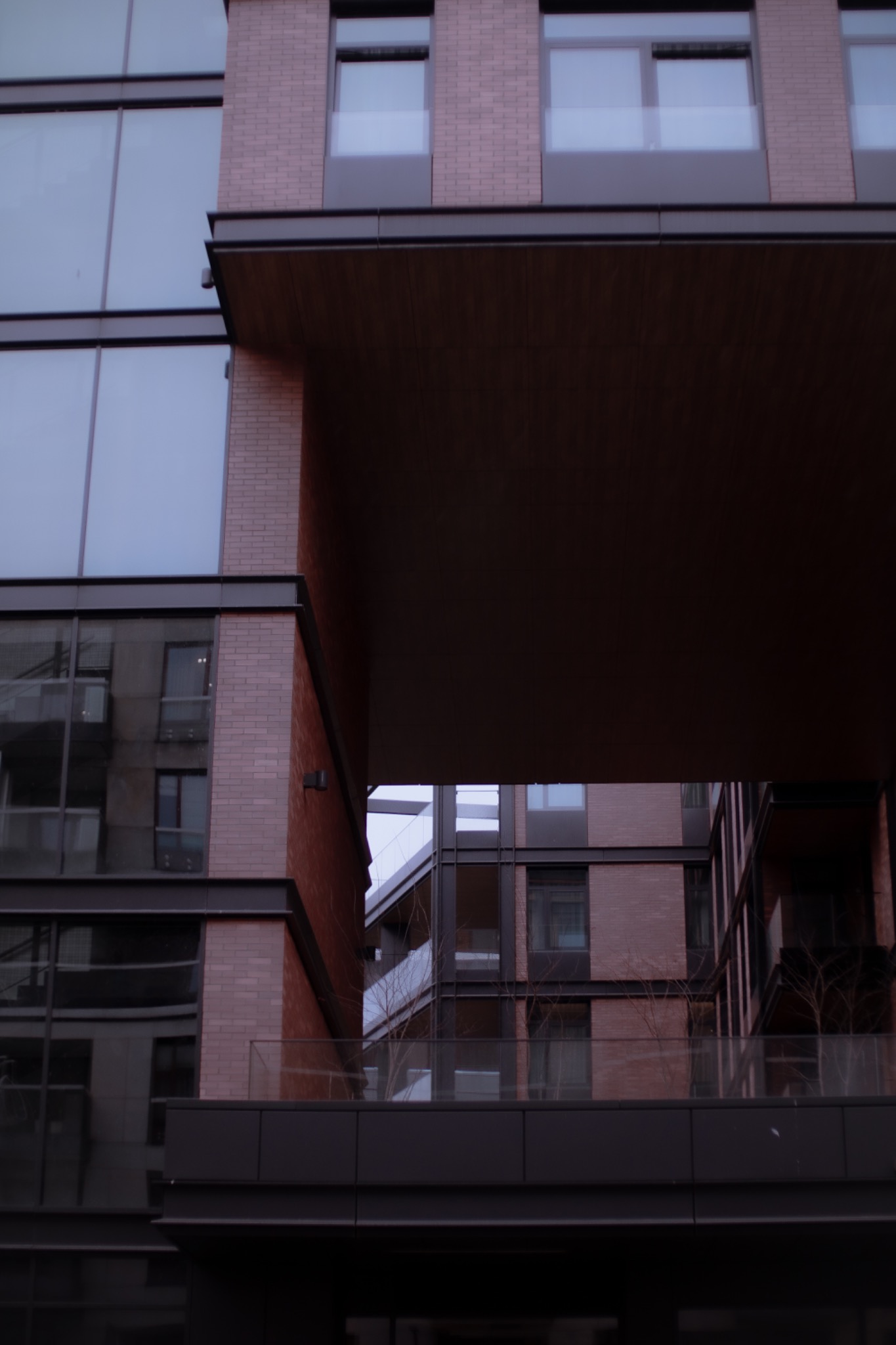 Nowoczesny budynek mieszkalny z ceglaną fasadą i dużymi oknami, widziany z dołu. Zwraca uwagę architektoniczne połączenie budynków.