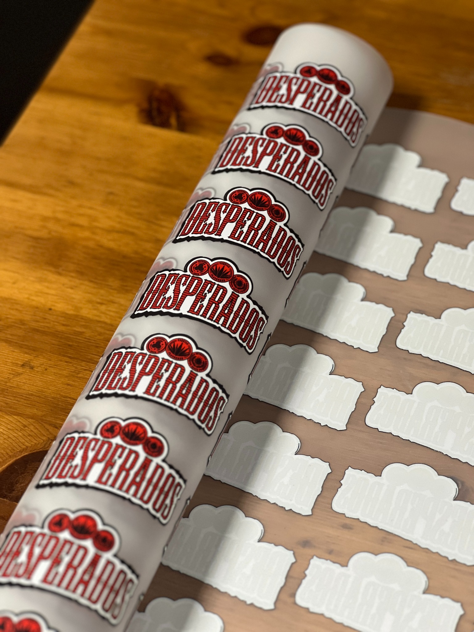 Rolka z nadrukiem 'Desperados' na folii transferowej, przygotowana do naniesienia na koszulki. Widoczne białe, puste przestrzenie po wyciętych wzorach.