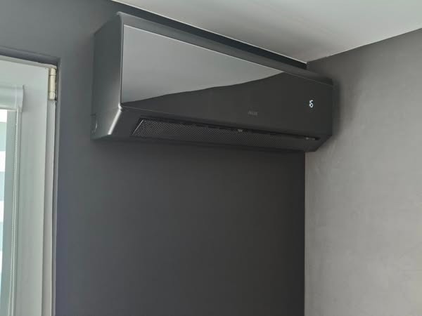 Czarny klimatyzator AUX na szarej ścianie, widoczny obok okna. Minimalistyczny design, nowoczesne wnętrze.