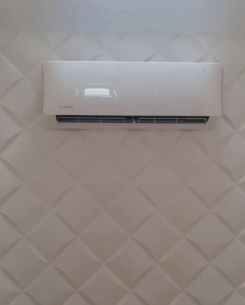 Biały klimatyzator na ścianie z dekoracyjnymi panelami 3D w kształcie rombów. Widoczny model marki 'SUTENKO'.