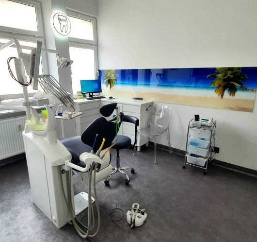 Nowoczesny gabinet dentystyczny z fotelem, narzędziami i dekoracją ścienną z motywem plaży. Jasne wnętrze, profesjonalne wyposażenie.