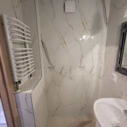 DEMIAN MISHCHUK Demli-BUD - Biała łazienka z marmurowymi płytkami, grzejnikiem drabinkowym i umywalką. Widoczny fragment lustra i kratka wentylacyjna. Minimalistyczny design, jasne oświetlenie.