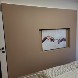 DEMIAN MISHCHUK Demli-BUD - Beżowa ściana z wnęką, w której umieszczono obraz 'Stworzenie Adama'. Nowoczesne oświetlenie sufitowe i fragment łóżka w dolnym rogu kadru.