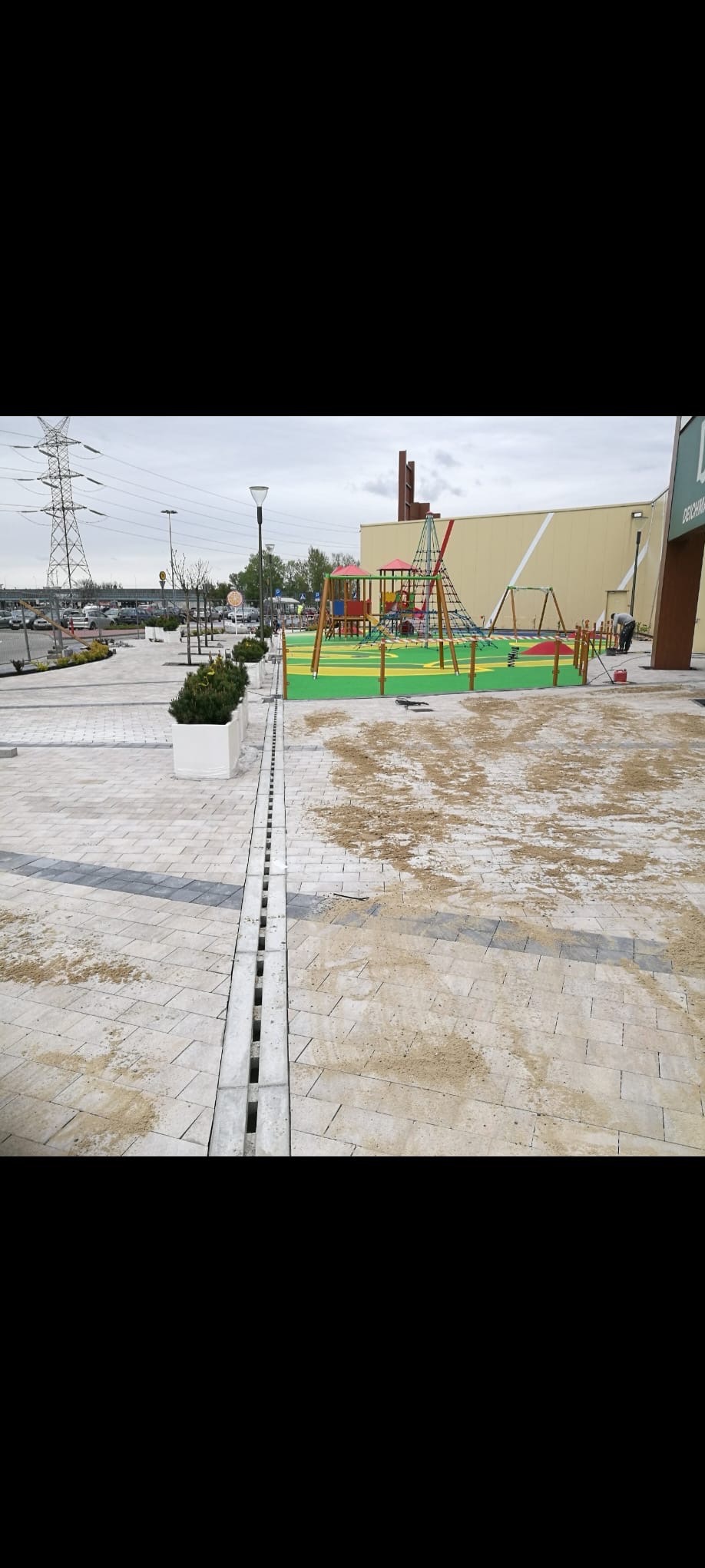 Układanie kostki brukowej na placu zabaw z widocznym systemem drenażowym i elementami placu zabaw w tle. Prace wykończeniowe, piasek na kostce.