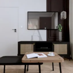 Nowoczesny salon z telewizorem, szafką RTV z rattanowymi frontami i stolikami kawowymi. Biało-brązowa ściana, lampa wisząca i zasłony w neutralnych barwach.