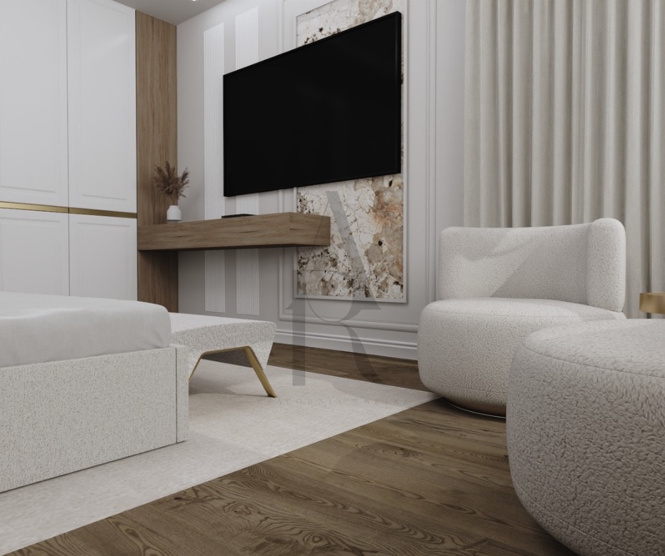 Nowoczesna sypialnia z telewizorem na ścianie, beżowym fotelem i pufą. Minimalistyczny design z drewnianą podłogą i białymi meblami.