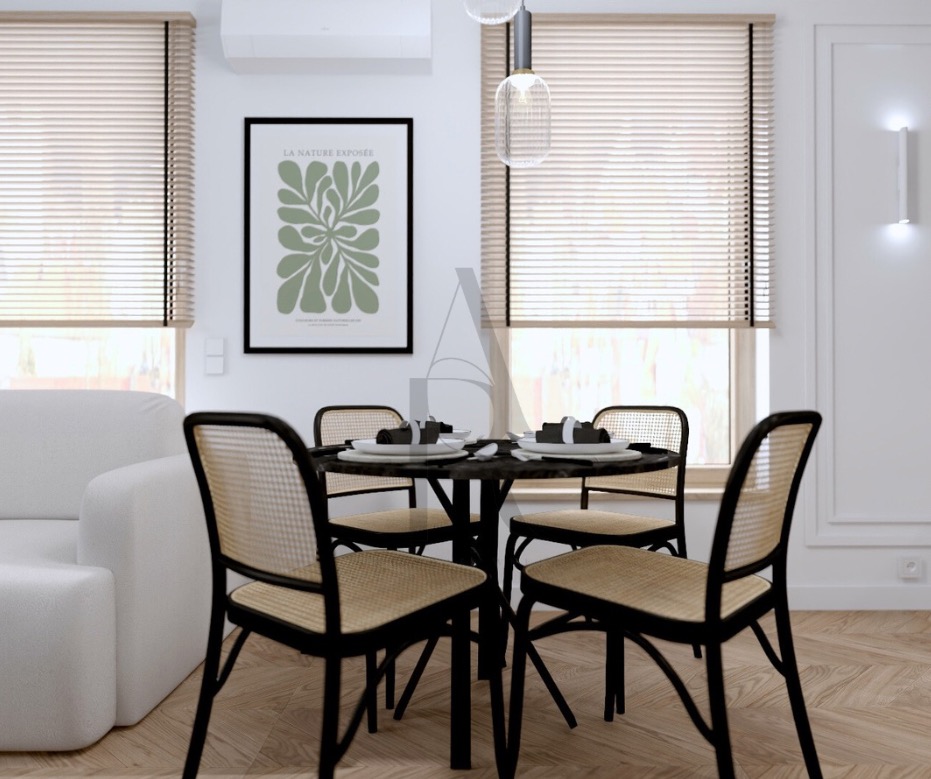 Jasne wnętrze jadalni z okrągłym stołem i czterema krzesłami z rattanu. Na ścianie plakat z motywem roślinnym, a w oknach jasne żaluzje.