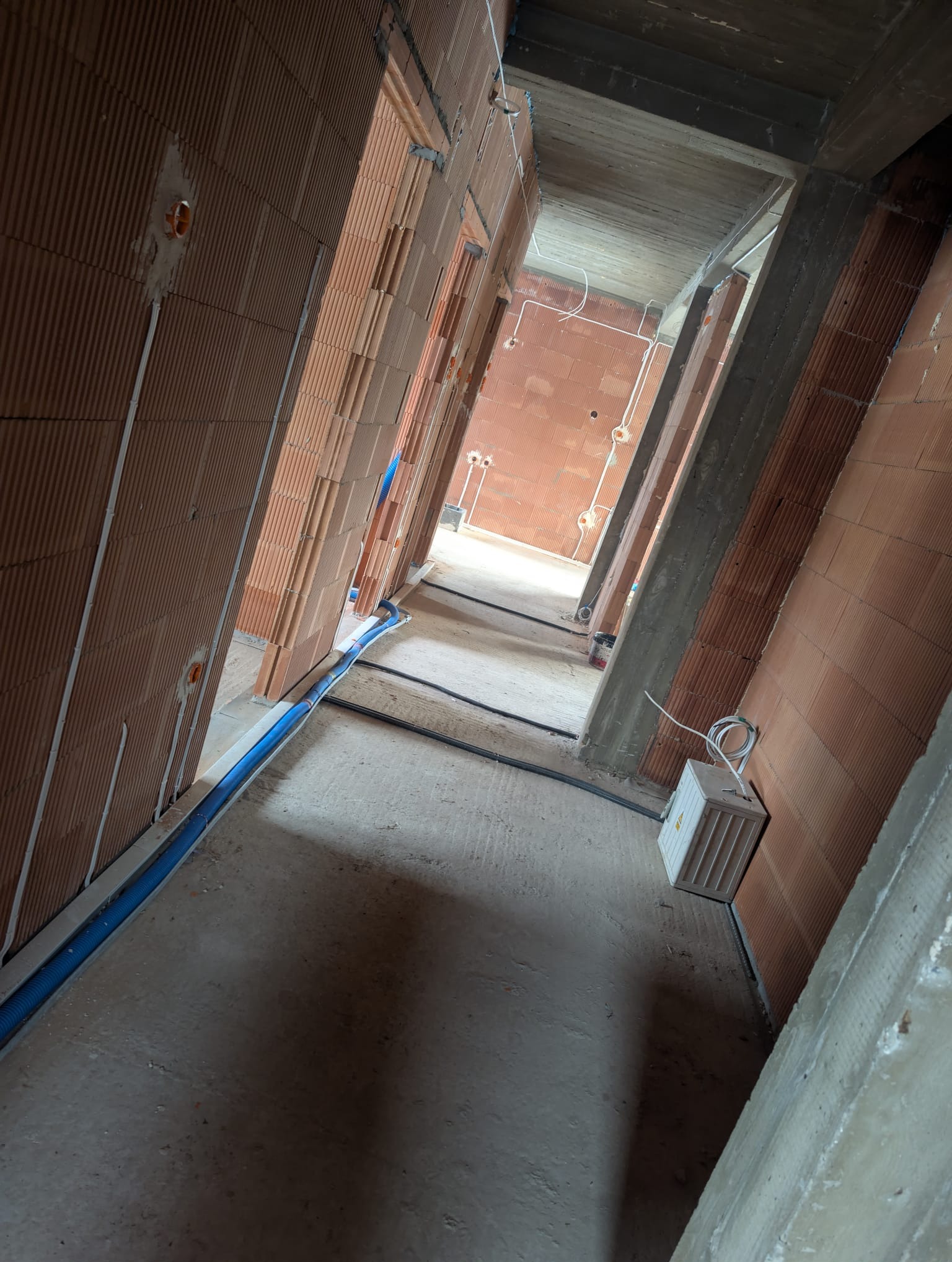 Wnętrze budynku w trakcie budowy. Widoczne ściany z cegły, instalacja elektryczna w peszlach i puszki elektryczne. Surowy stan, brak wykończenia.