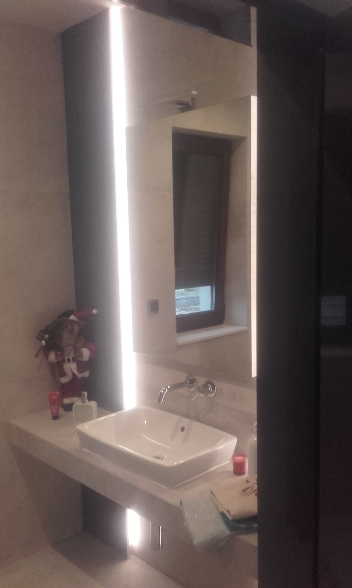 Nowoczesna łazienka z podświetlanym lustrem i białą umywalką nablatową. Dekoracja świąteczna dodaje unikalnego charakteru wnętrzu.