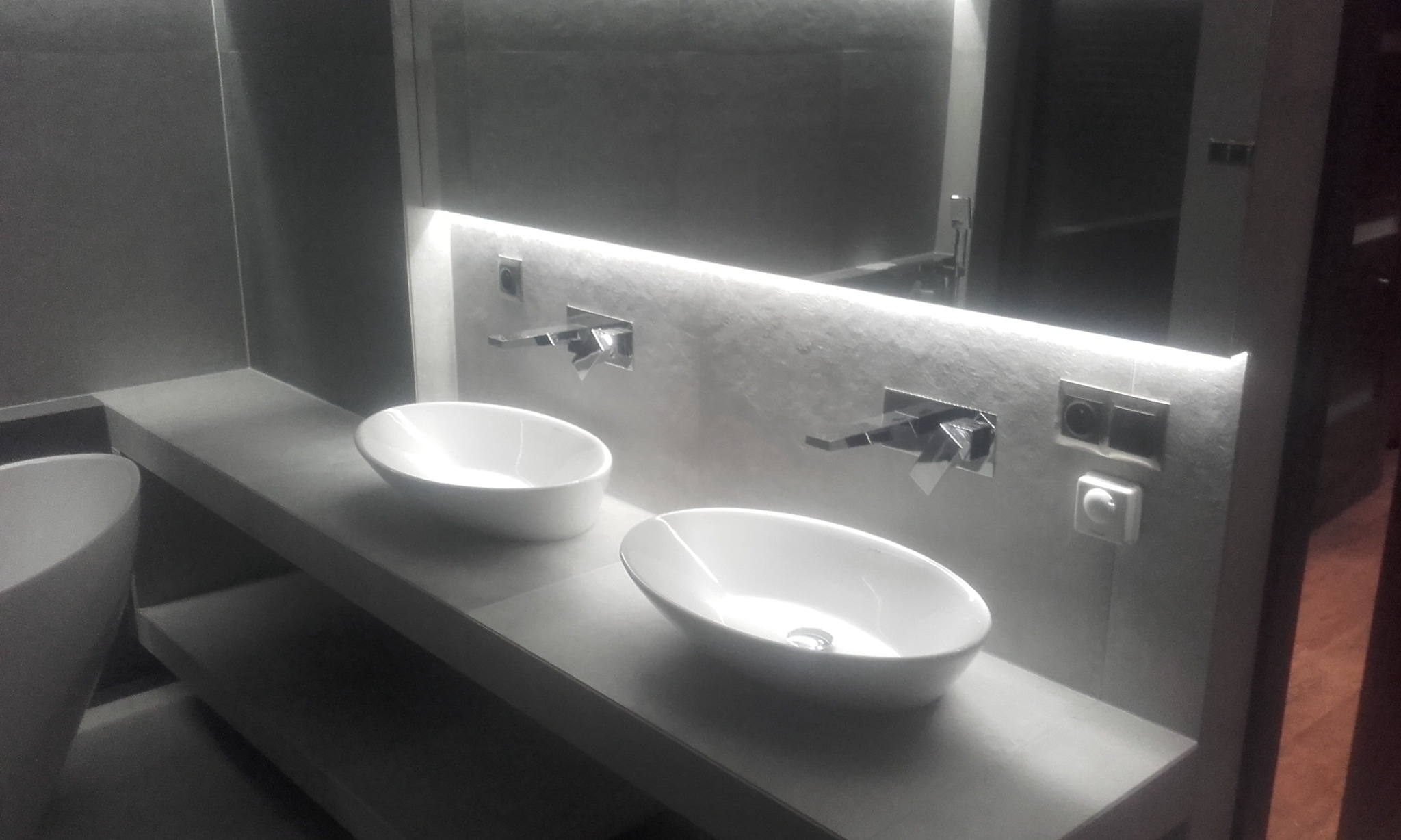 Nowoczesna łazienka w odcieniach szarości z dwiema owalnymi umywalkami, minimalistyczną armaturą i podświetlanym lustrem, tworząca elegancką i funkcjonalną przestrzeń.