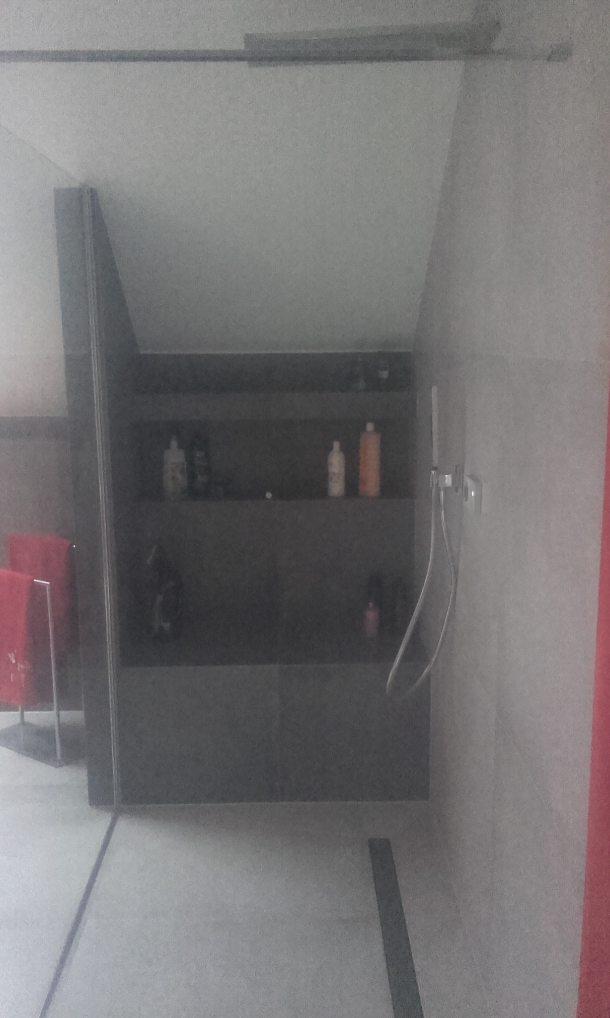 Nowoczesna kabina prysznicowa z szarymi płytkami, półkami wnękowymi i minimalistycznym odpływem liniowym. Widoczne kosmetyki i ręcznik.