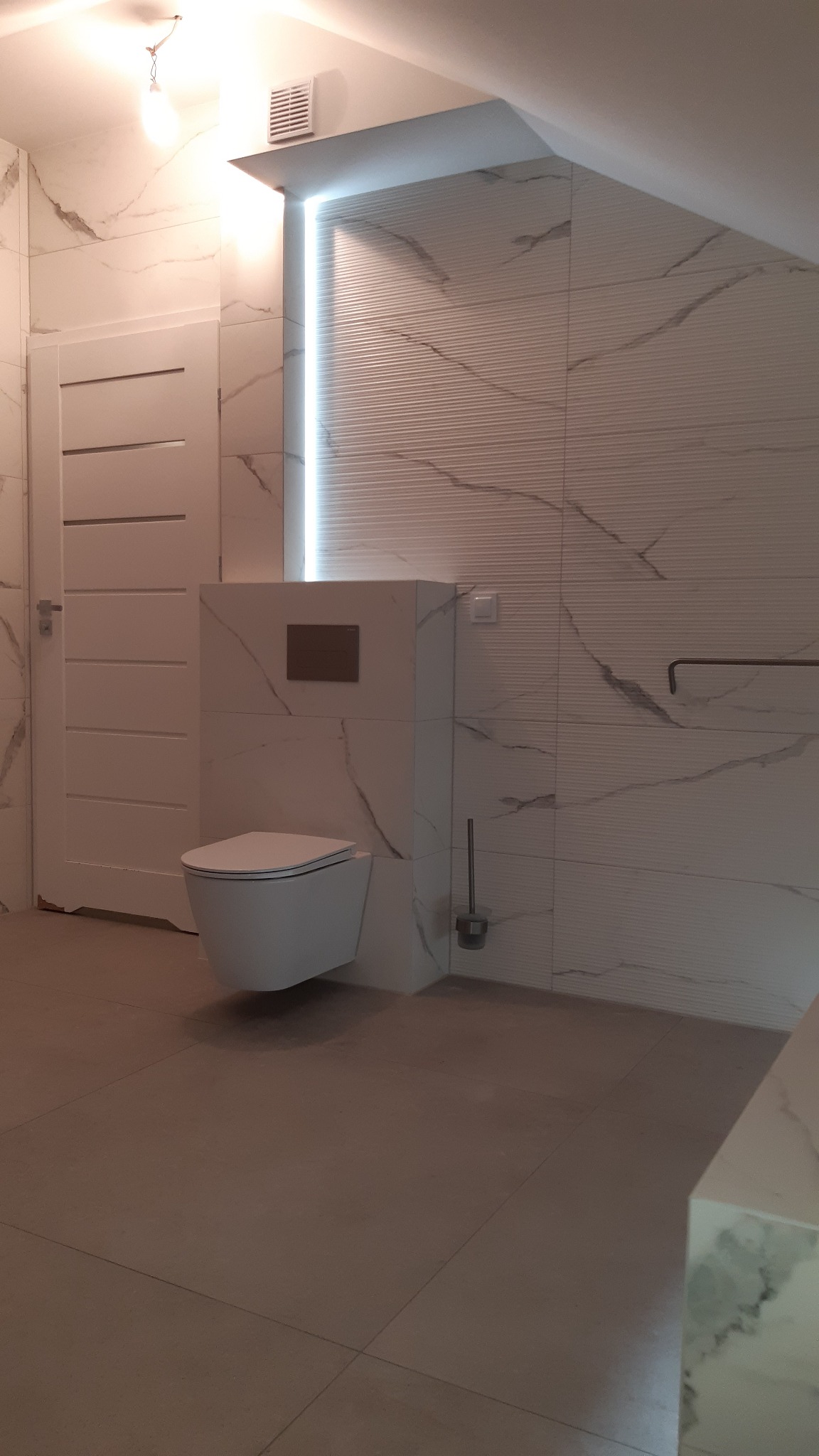 Nowoczesna łazienka z podświetleniem LED, białą armaturą i płytkami imitującymi marmur. Uwagę przykuwa minimalistyczny design i dbałość o detale.