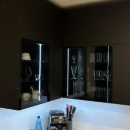 Nowoczesna, czarna kuchnia z podświetlanymi szklanymi witrynami, drewnianymi frontami i czarnym blatem. Na blacie ekspres do kawy i akcesoria kuchenne.