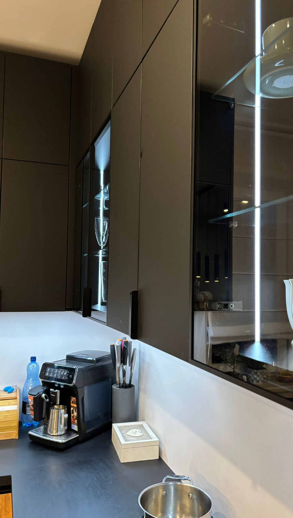 Nowoczesna kuchnia z czarnymi szafkami, oświetleniem LED wewnątrz, szklanymi frontami i blatem. Na blacie ekspres do kawy i akcesoria kuchenne.