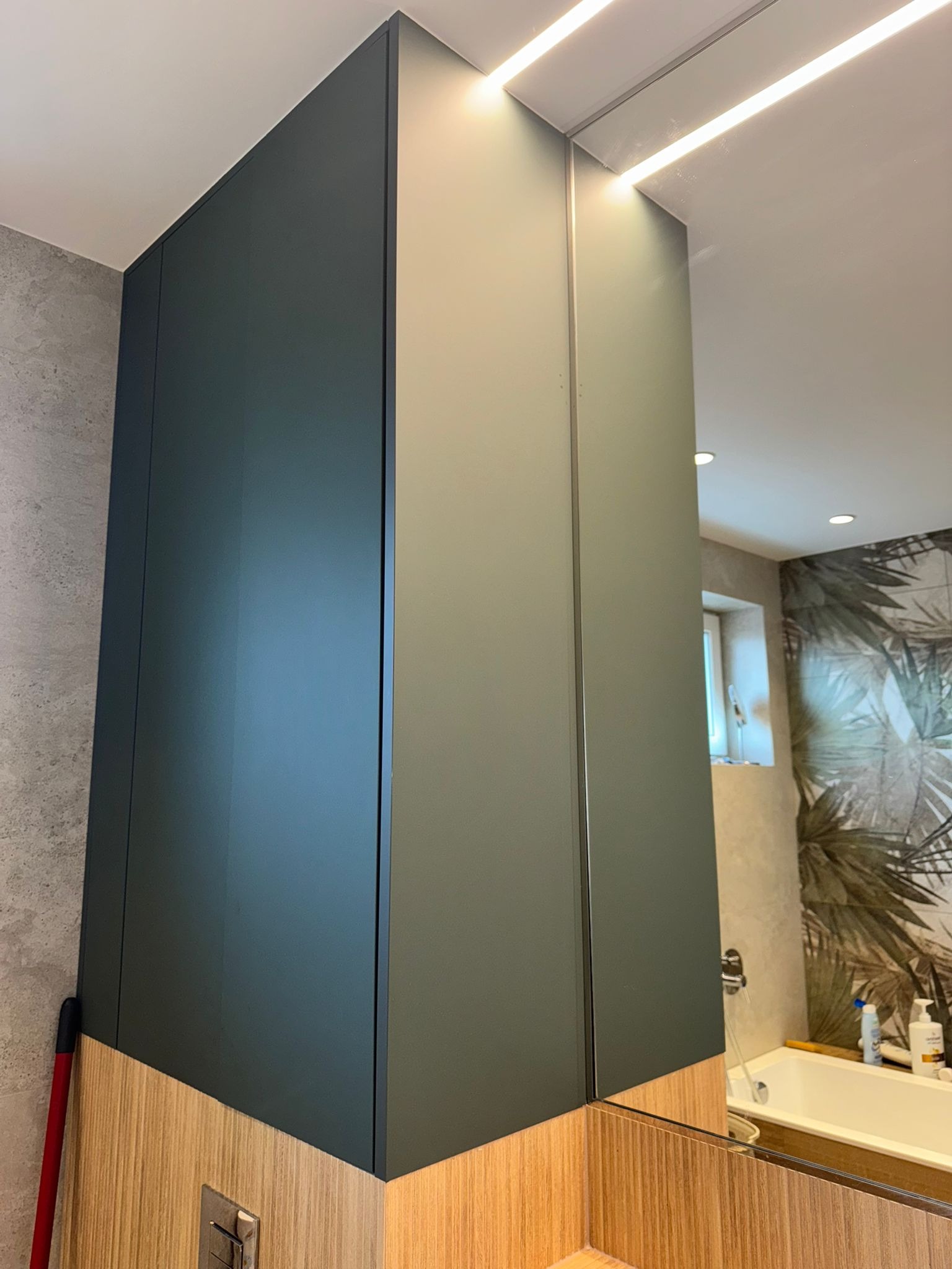 Nowoczesna szafka łazienkowa z lustrzanymi drzwiami i oświetleniem LED w Bielsko-Białej. Ciemny odcień frontów i drewnopodobny cokół.