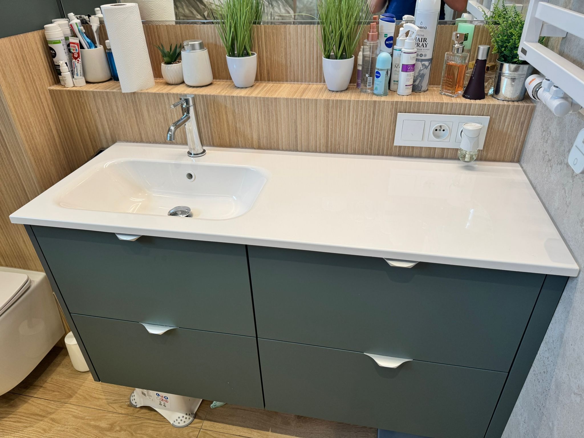 Nowoczesna szafka łazienkowa w odcieniach szarości z białą umywalką i blatem. Nad nią półka z akcesoriami łazienkowymi i dekoracjami. Minimalistyczny design.