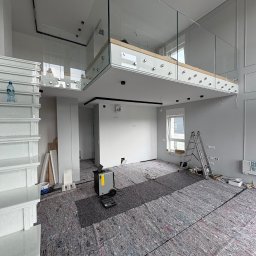 Inspektor Iskra - Wnętrze w trakcie remontu: zabezpieczona podłoga, drabina, schody z butelką wody i szklana balustrada antresoli z punktowym oświetleniem sufitowym.