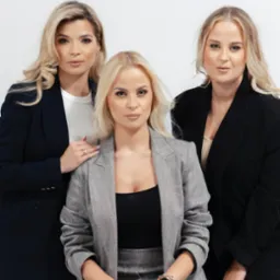 Profesjonalny portret grupowy trzech kobiet w garniturach na białym tle, z subtelnym makijażem, Białystok. Kobieta na środku siedzi, pozostałe stoją.