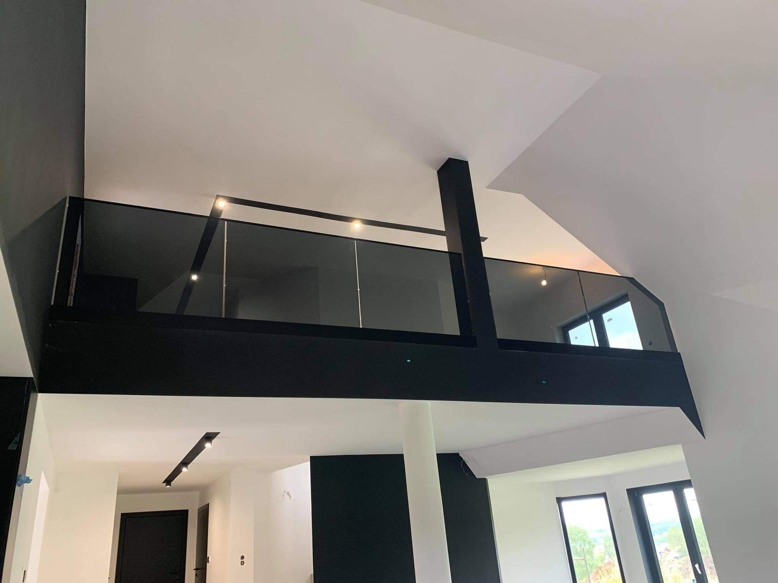 Nowoczesna, czarna balustrada szklana na antresoli z oświetleniem punktowym, widok z dołu, w tle okna i minimalistyczne wnętrze w bieli i czerni.