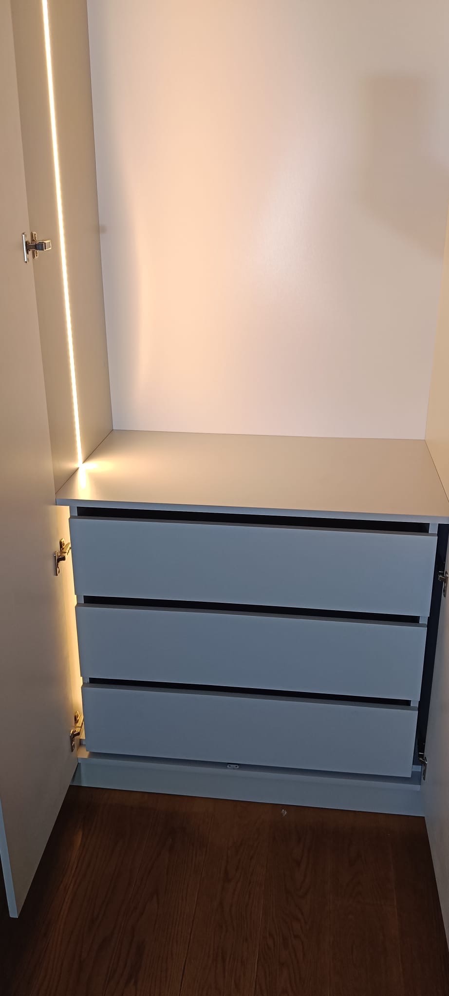 Wnętrze szafy wnękowej z trzema szufladami w odcieniach szarości. Oświetlenie LED podkreśla minimalistyczny design i funkcjonalność mebla.