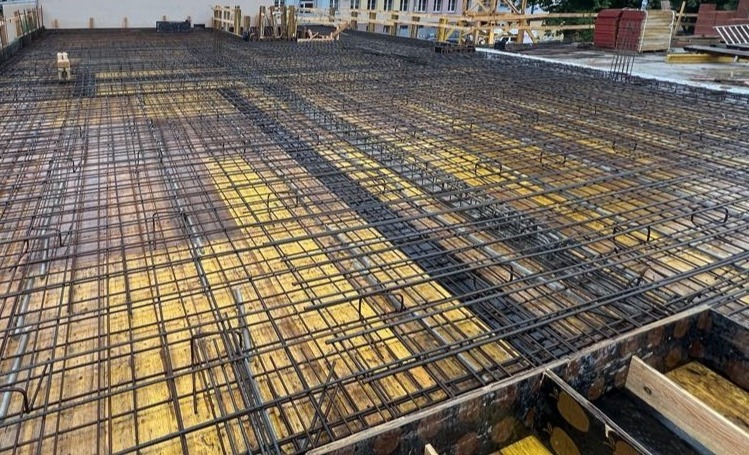 Siatka zbrojeniowa na deskowaniu, przygotowana do zalania betonem. Widoczne elementy konstrukcyjne i detale zbrojenia. Ujęcie z góry, perspektywa szerokokątna.