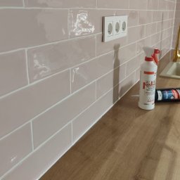 Dav-Bau Dawid Górecki - Położone, błyszczące, różowe płytki w kuchni, z białą fugą i gniazdkiem elektrycznym. Na blacie leżą preparaty do czyszczenia fug.