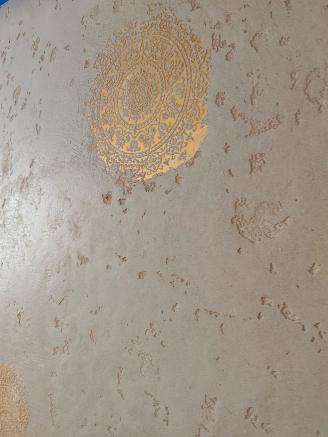 Beżowa ściana z dekoracyjnym, złocistym ornamentem mandali i wyraźną fakturą. Unikalne wykończenie wnętrza z efektem postarzenia i ręcznie nakładanym wzorem.