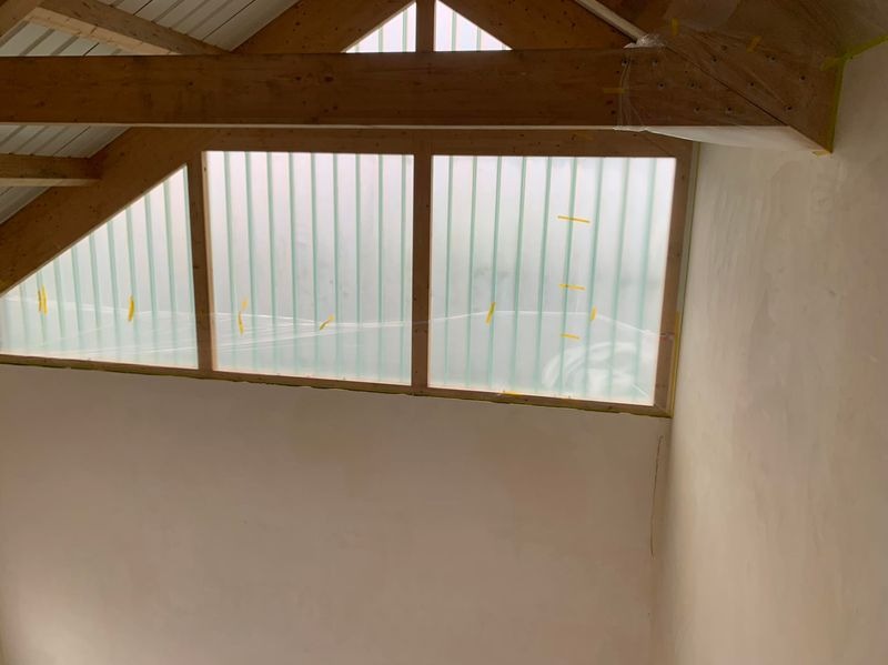 Poddasze po nałożeniu gładzi, zabezpieczone okna dachowe z widoczną konstrukcją drewnianą i metalowym dachem. Ściany przygotowane do malowania.