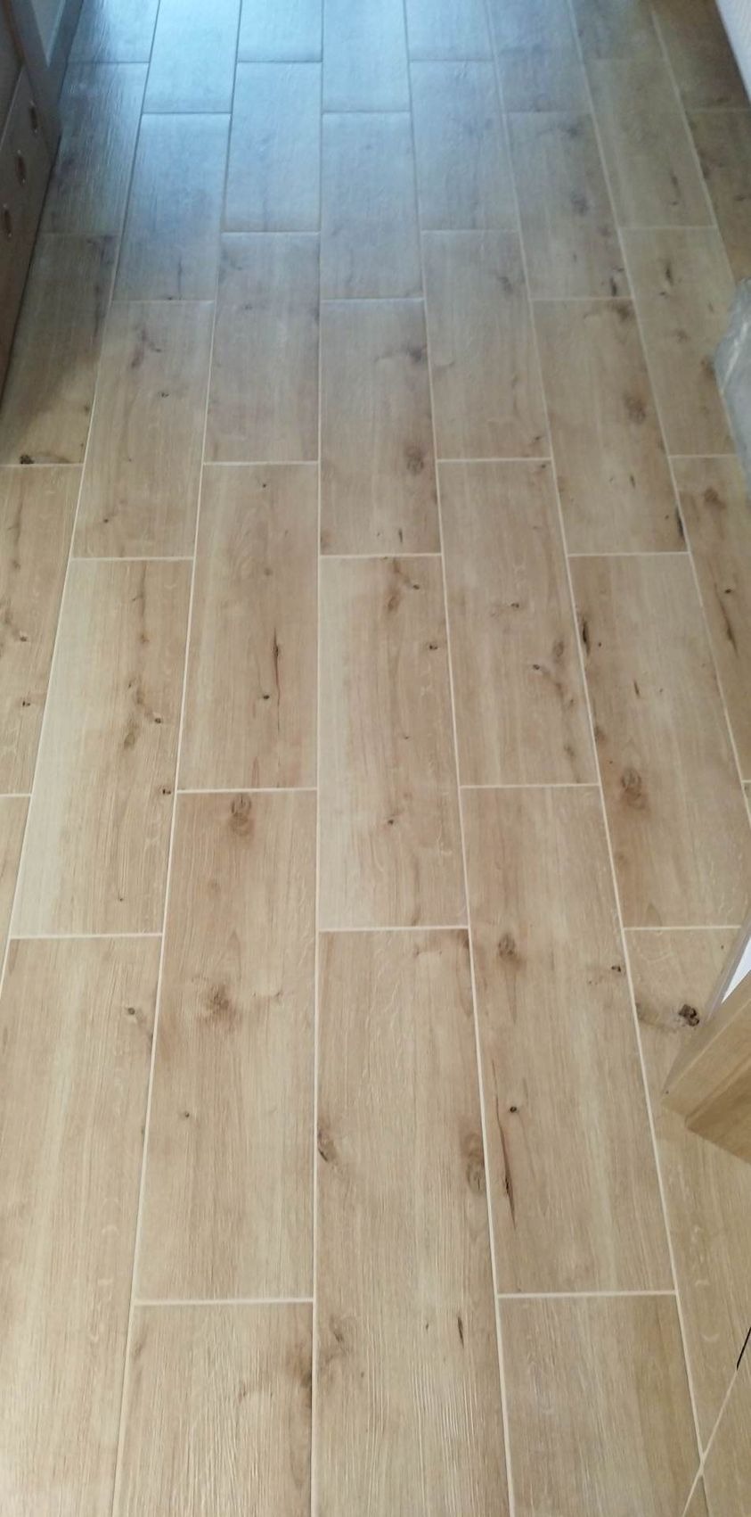 Ułożona podłoga z płytek imitujących drewno w Sosnowcu. Jasne, prostokątne płytki z wyraźnym rysunkiem słojów, ułożone w regularny wzór. Widoczne fugi.