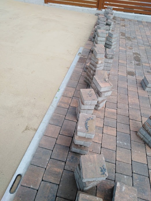 Ułożona kostka brukowa w trakcie prac, widoczny fragment podsypki piaskowej i poziomica. Część kostki ułożona, część w stosach, gotowa do montażu.