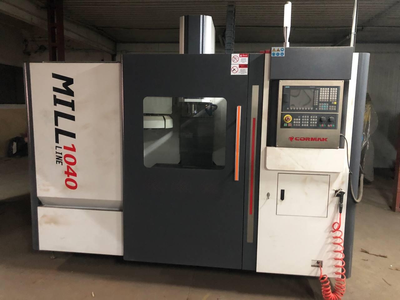 Szara frezarka CNC MILL LINE 1040 z panelem sterowania CORMAK, widoczna w hali produkcyjnej, z przewodem pneumatycznym zwisającym z boku.