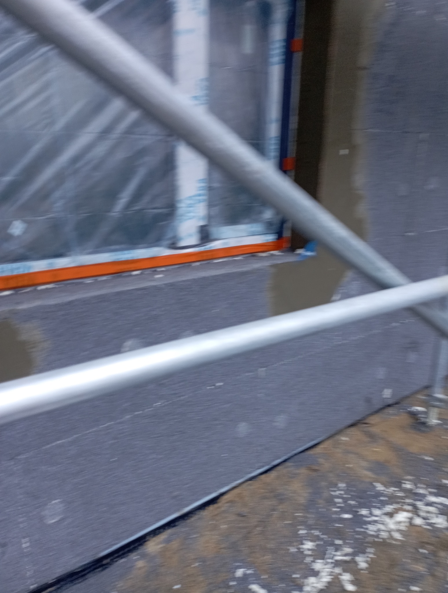 Szare ocieplenie budynku styropianem grafitowym, widoczne rusztowanie i okno zabezpieczone folią. Detal izolacji termicznej budynku.