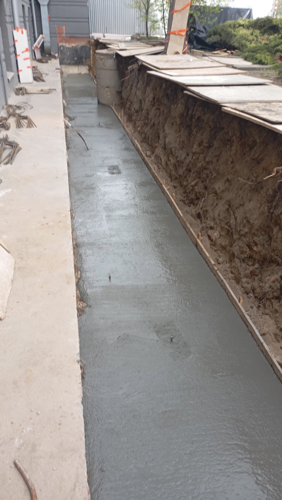 Wylany fundament z szalunkiem, widoczne przygotowania do izolacji. Beton świeżo wylany, równomiernie rozprowadzony. Widok z góry na dół, z bliska, z boku budynku.