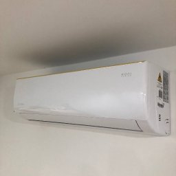 YURII STANOVYCH CoolCentral - Biała klimatyzacja z subtelnym złotym akcentem na górnej krawędzi, zamontowana na jasnej ścianie w pomieszczeniu. Widoczne detale obudowy i oznaczenia producenta.