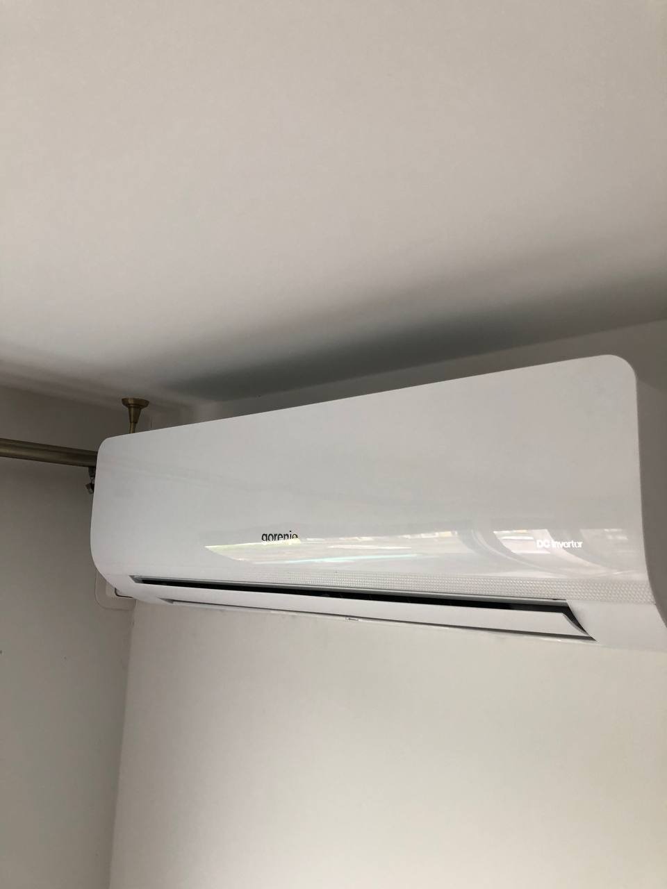 Biała klimatyzacja Gorenje DC Inverter zamontowana na ścianie, widoczna rurka instalacyjna i fragment sufitu. Minimalistyczny design.