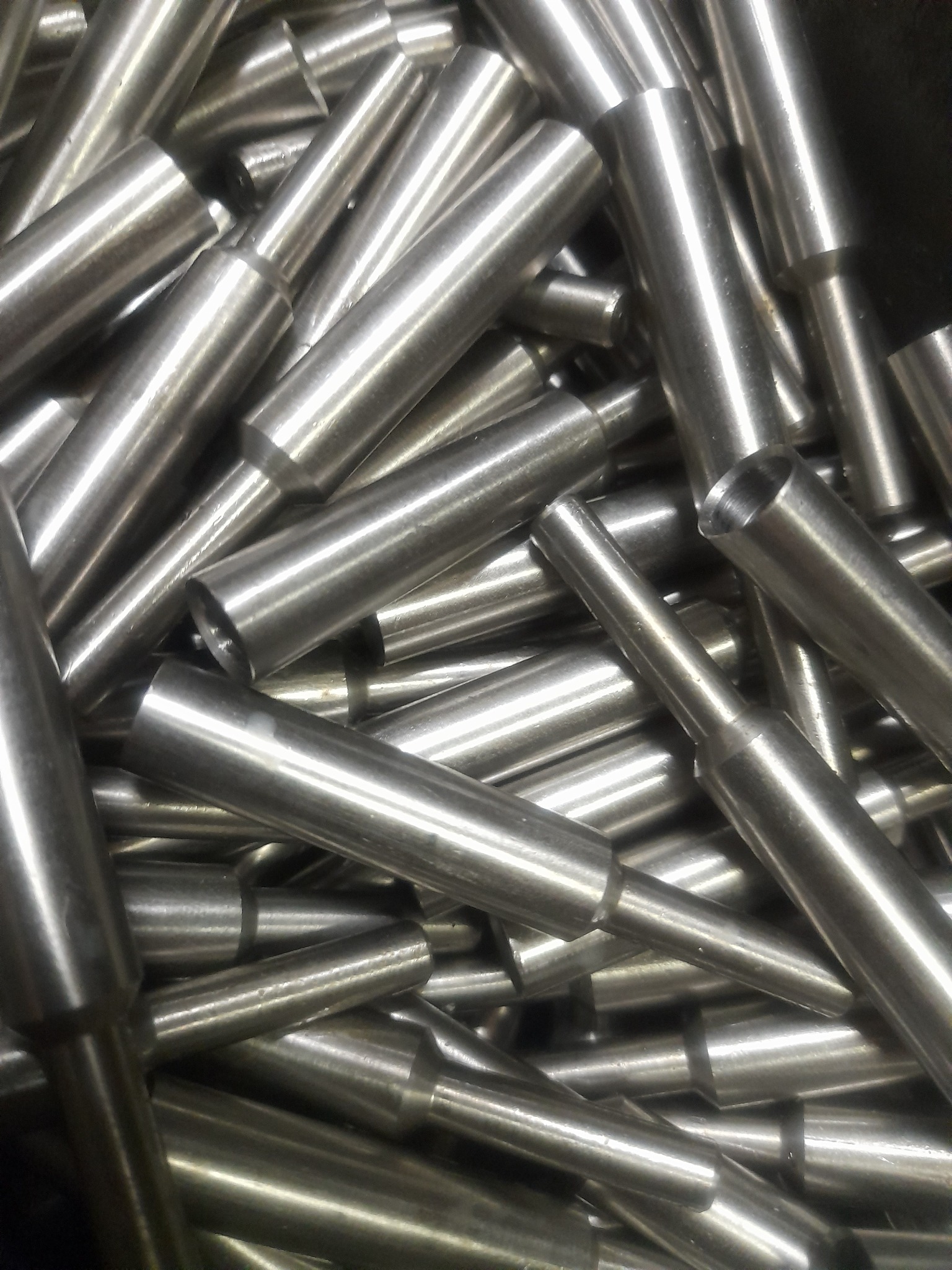 Stalowe, precyzyjnie wytoczone elementy z otworem, ułożone chaotycznie, ukazujące metaliczny połysk i dokładność wykonania.