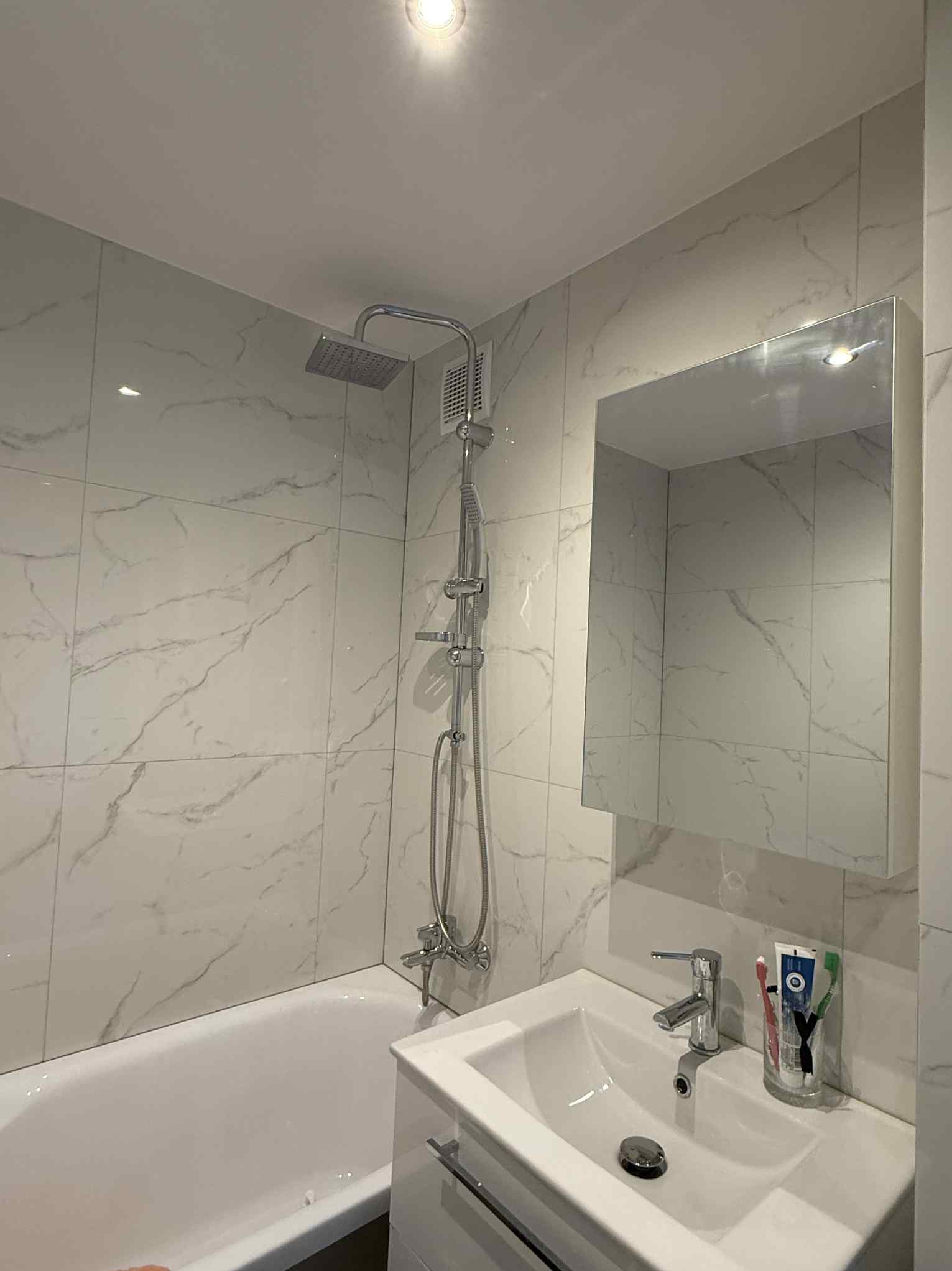 Biała łazienka po remoncie: marmurowe płytki, bateria prysznicowa z deszczownicą, umywalka z szafką i lustro. Minimalistyczny design, jasne oświetlenie.