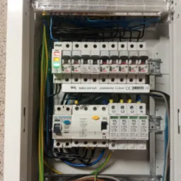Rozdzielnica elektryczna wewnątrz domu po modernizacji. Widoczne zabezpieczenia RCD i ochronnik przepięciowy, okablowanie i bezpieczniki.