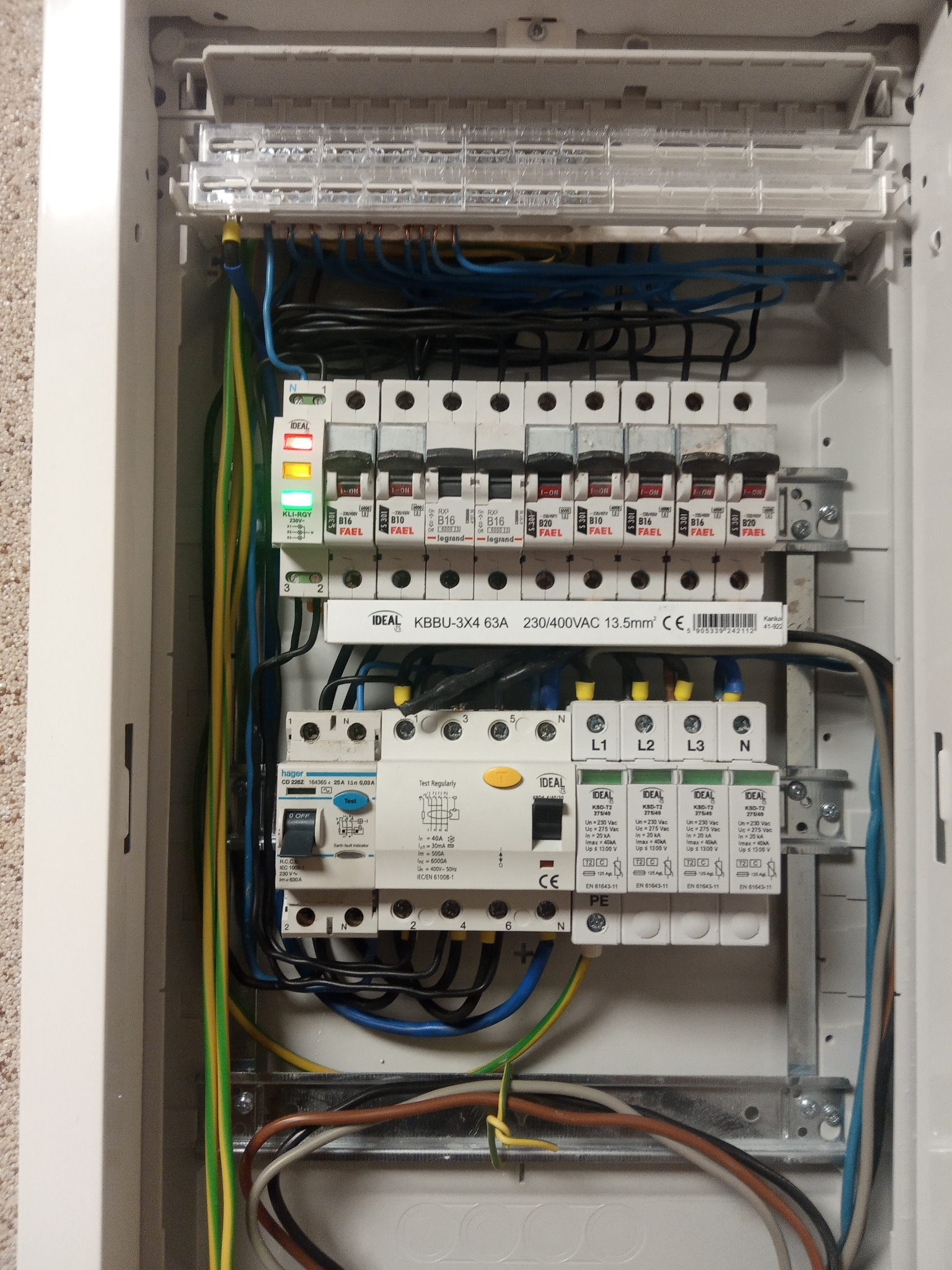 Rozdzielnica elektryczna wewnątrz domu po modernizacji. Widoczne zabezpieczenia RCD i ochronnik przepięciowy, okablowanie i bezpieczniki.