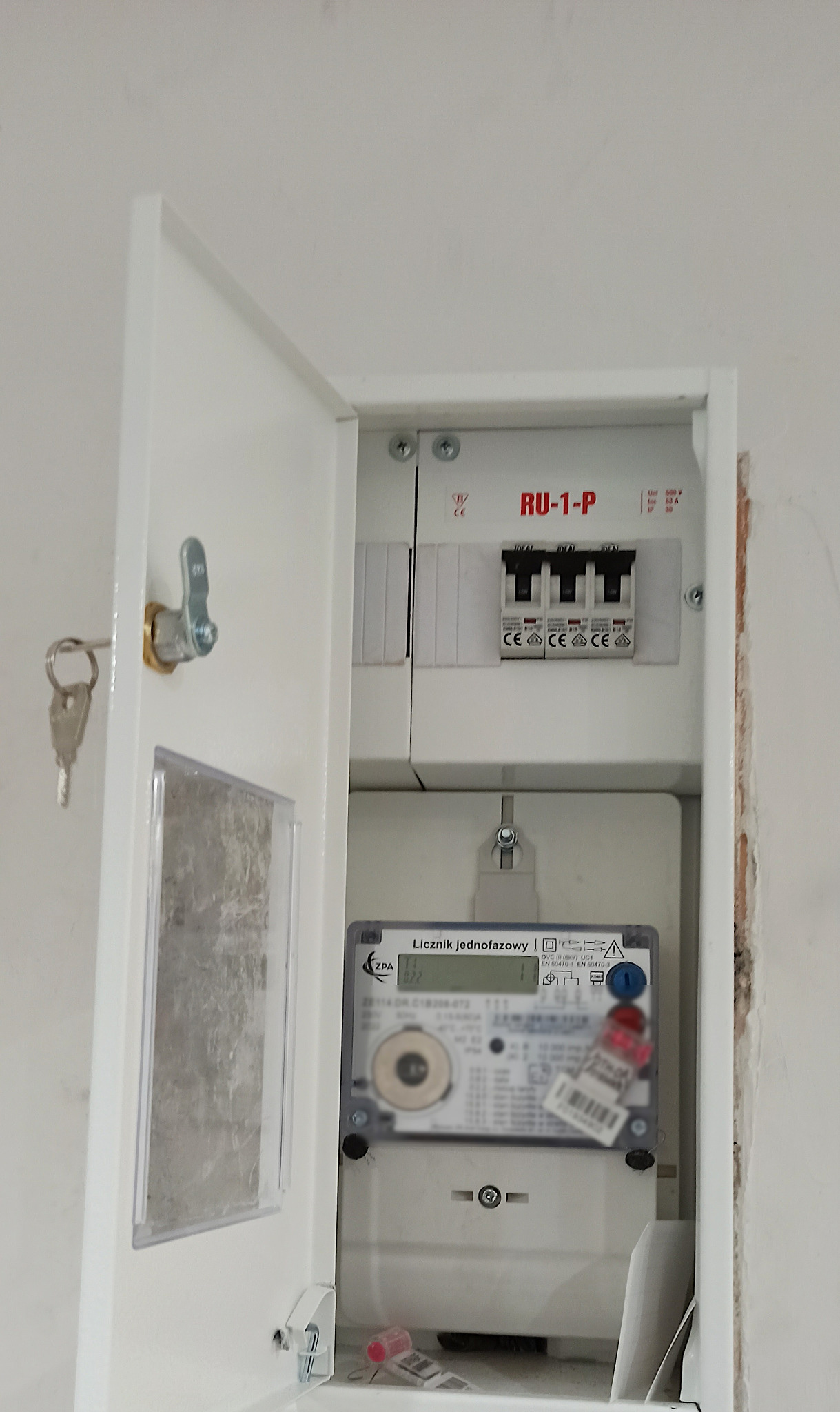 Otwarta skrzynka elektryczna z licznikiem jednofazowym ZPA i zabezpieczeniami RU-1-P, widoczne klucze. Modernizacja zabezpieczeń w mieszkaniu.
