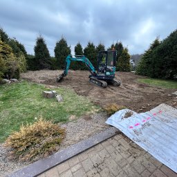 Drakop - Niebieska mini koparka Sunward na częściowo wyrównanym terenie działki, z widocznymi śladami pracy i zielenią w tle, pod pochmurnym niebem.