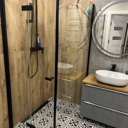 Svitlana Krysa - Nowoczesna łazienka z kabiną prysznicową typu walk-in, drewnopodobnymi płytkami ściennymi i wzorzystą podłogą. Umywalka nablatowa i okrągłe lustro z podświetleniem.