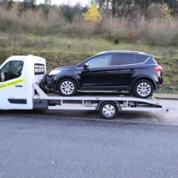 Laweta z czarnym Fordem Kuga na platformie, zaparkowana na asfalcie, z napisem 'Pomoc Drogowa' i numerem telefonu na kabinie.