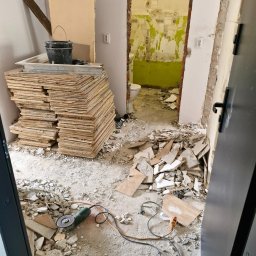 Serhii popenko - Po demontażu: sterta płyt, gruz i szlifierka kątowa w pomieszczeniu z widoczną, odartą ścianą w tle. Otwarta przestrzeń po wyburzeniu.