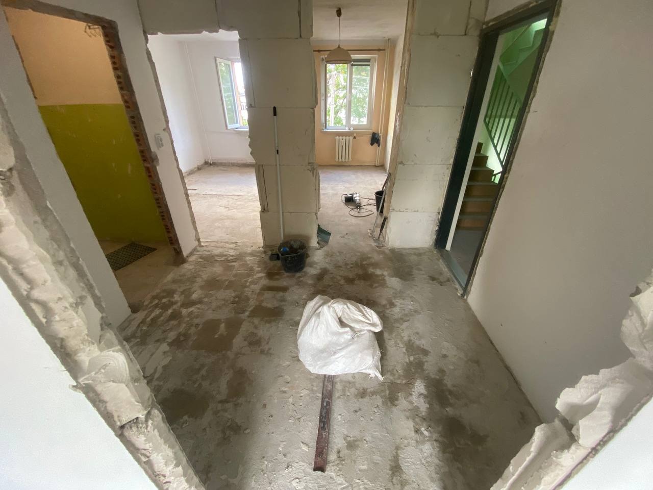 Wnętrze w trakcie prac rozbiórkowych: usunięte ściany działowe, widoczne gruz i worki. Otwarta przestrzeń z widokiem na schody i okna.
