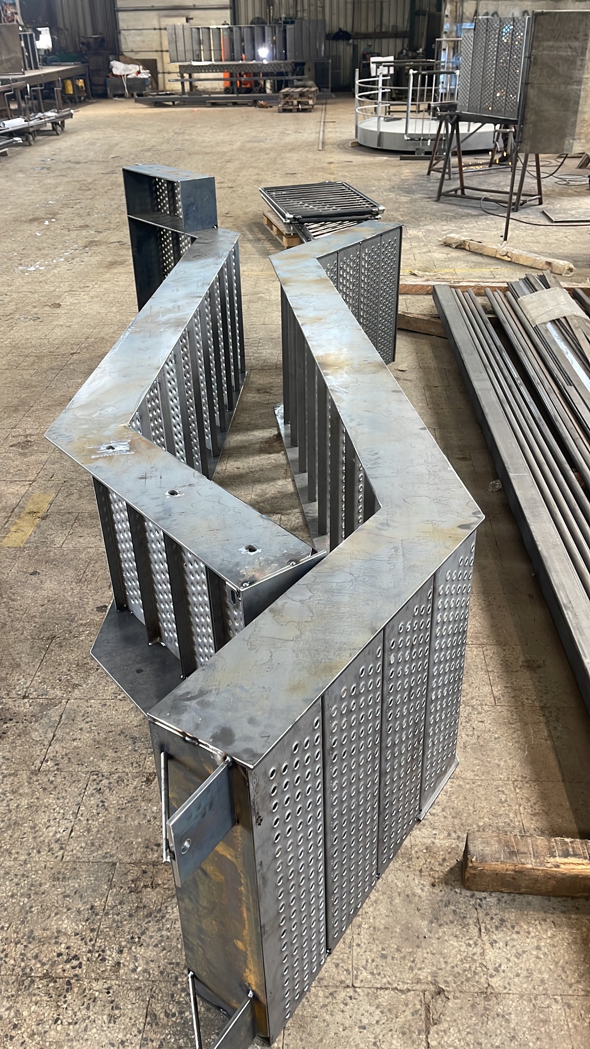Surowa, metalowa konstrukcja w kształcie litery Z z perforowanymi ścianami, w hali produkcyjnej. Widoczne ślady obróbki i spawania, elementy w trakcie montażu.