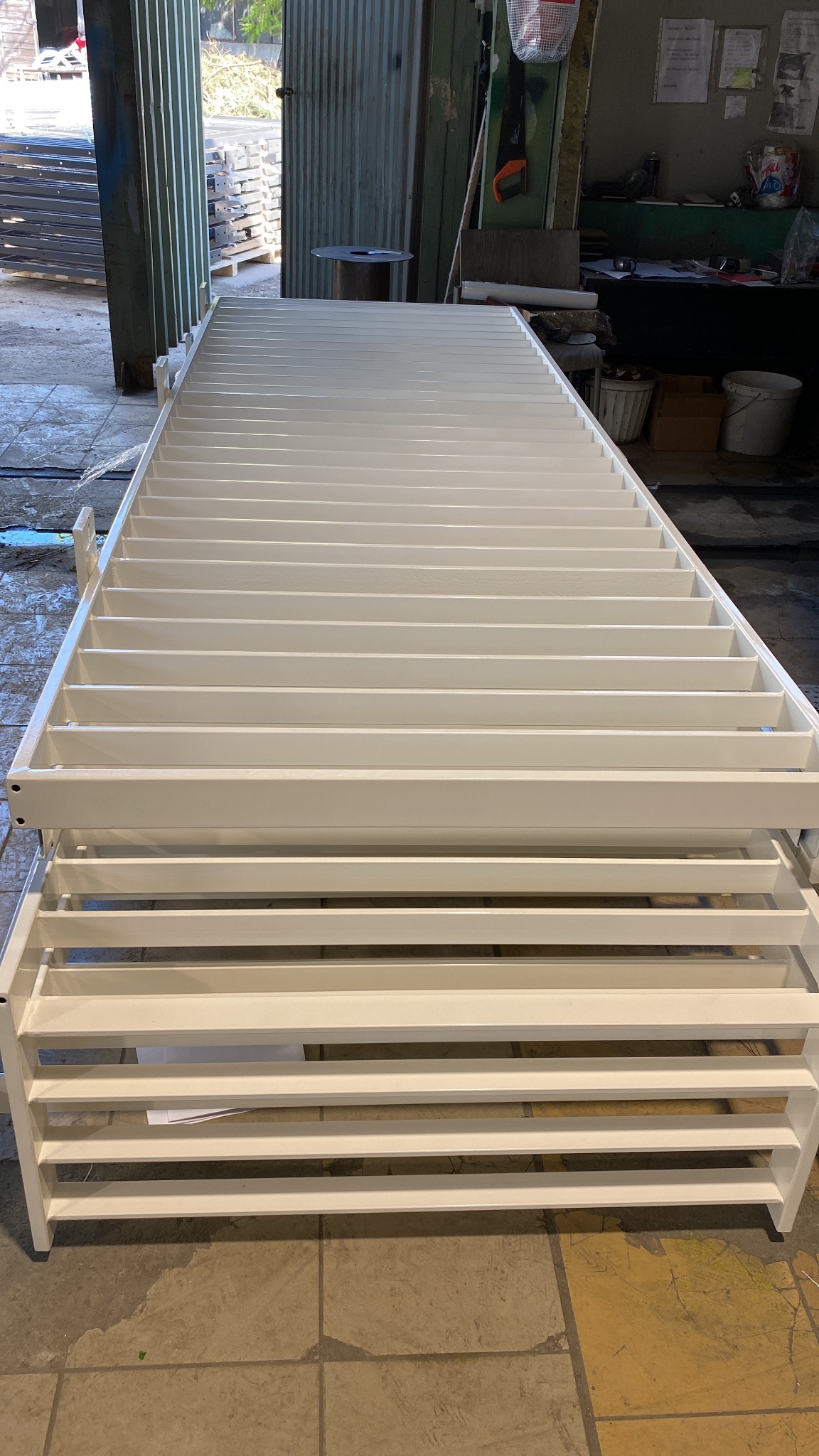 Biała, metalowa konstrukcja kratowa, prawdopodobnie element balustrady lub ogrodzenia, w warsztacie. Widoczne spawane łączenia i świeża farba.