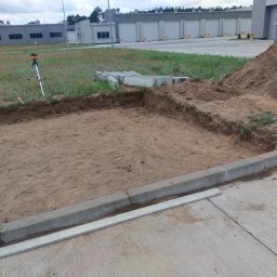 Kewin kuciarski - Przygotowanie terenu pod posadzkę: wykop z piaskiem, obrzeża z betonowych krawężników, niwelator laserowy na statywie, sterta ziemi w tle.