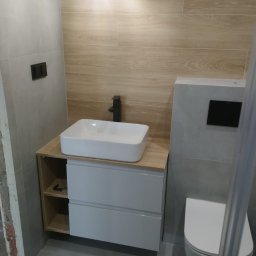 EXECUTIVE COOPERATION COMPANY E.C.C_D&S - Nowoczesna łazienka po remoncie: biała umywalka nablatowa z czarną armaturą, drewnopodobne płytki ścienne, szara podłoga i wisząca toaleta. Minimalistyczny design.